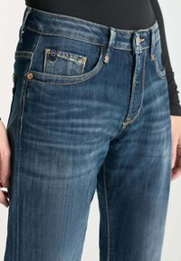 Jeans de mezclilla azul oscuro con una textura suave, que cuentan con un cierre de botones tradicional, bolsillos frontales y detalles de desvanecimiento sutil.