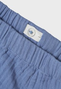 Blå texturerad tyg med en rynkad midja och knäppning. Midjebandet har ett vitt elastiskt band.