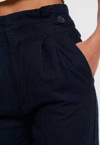 Námořnické modré kalhoty vyrobené z texturované tkaniny, s knoflíkovým zapínáním, plochým předním dílem a bočními kapsami pro zvýšení funkčnosti.