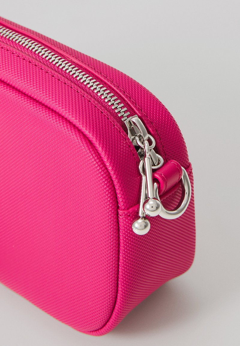 Fuchsia roze ritszakje gemaakt van gestructureerd nylon, met een zilveren rits en hardware, afgeronde hoeken en een compact ontwerp.