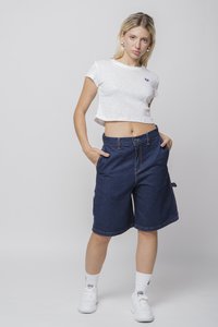 Hvit avkortet t-skjorte med et lilla hjerte-design, kombinert med mørkeblå denim shorts med sidelommer og en avslappet passform. Hvite sneakers.