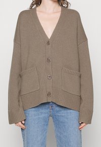 Strickjacke in Taupe mit V-Ausschnitt, fünf Knöpfen und Fronttaschen. Mit übergroßen Ärmeln und cropped Saum. Strukturmaterial, gemütlich und warm.