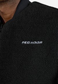 Giacca in pile nera con superficie texturizzata. Presenta un colletto a coste e la parola "PEGADOR" ricamata in bianco.