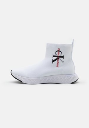 White knit sock sneaker with black and red "CK Calvin Klein Jeans" logo, textured white sole, and pull tab at the ankle.