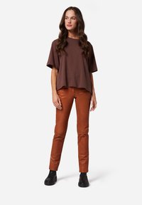 Bruine oversized t-shirt met korte mouwen, gecombineerd met slim-fit roestkleurige broek. Model draagt zwarte enkellaarzen. Eenvoudig, casual ontwerp.