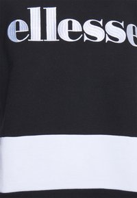Svart sweatshirt med en framträdande vit och ljusblå "ellesse" logotyp, samt ett vitt horisontellt band i botten. Mjuk, texturerad tyg.