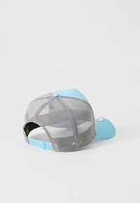 Gorra de camionero con la parte frontal azul claro y la parte trasera de malla gris. Cuenta con una visera curvada y una correa ajustable de plástico. Parche de logo en la parte trasera.