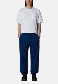 T-shirt bianco a maniche corte con taschino sul petto, abbinato a pantaloni navy con cordino. Scarpe sportive nere completano l'outfit.
