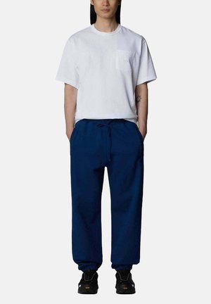 T-shirt bianco a maniche corte con taschino sul petto, abbinato a pantaloni navy con cordino. Scarpe sportive nere completano l'outfit.
