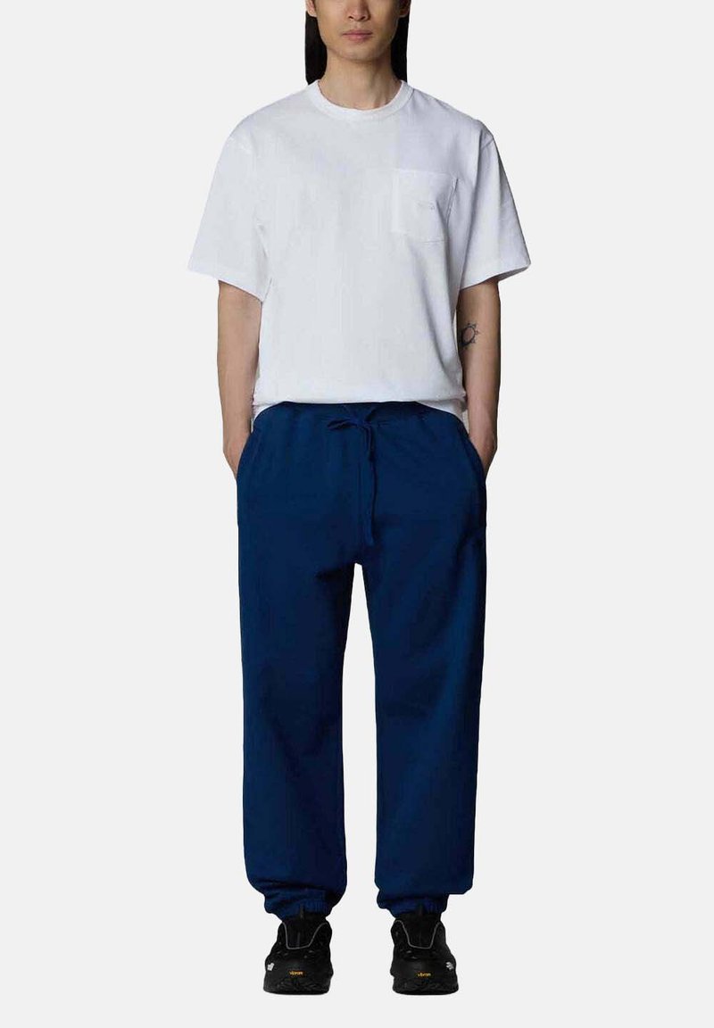 T-shirt bianco a maniche corte con taschino sul petto, abbinato a pantaloni navy con cordino. Scarpe sportive nere completano l'outfit.