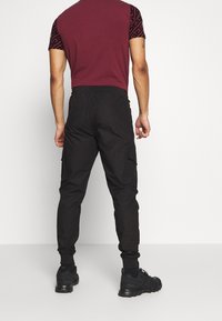 Zwarte cargobroek met elastische boorden, voorzien van zijzakken, gecombineerd met een bordeaux-rode fitted shirt met gestreepte zwarte mouwen.