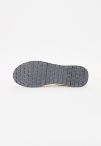 Suola di scarpa in gomma grigia con motivo di presa testurizzato. Forma solida e piatta, progettata per la trazione. Presenta indentazioni circolari e quadrate.