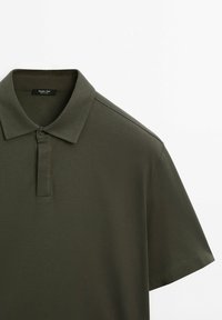 Polo vert foncé à manches courtes avec col, patte de boutonnage à un seul bouton et texture de tissu lisse.