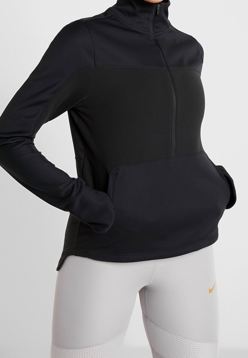 Svart atletisk pullover med hög krage, dragkedja framtill och sidofickor. Tillverkad av mjukt, stretchigt material med en kontrasterande övre panel.