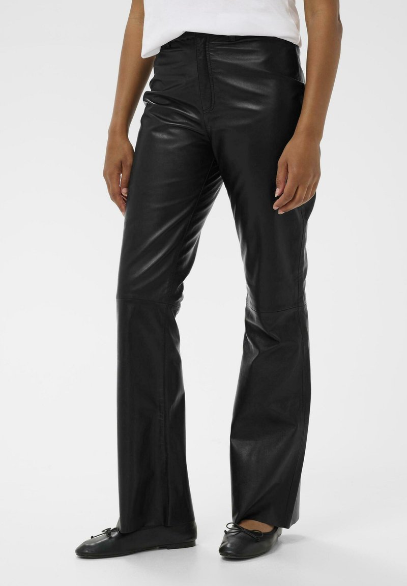Pantalons en cuir noir avec une taille ajustée et des jambes évasées. Texture lisse, matériel minimal et détails de couture contrastants.