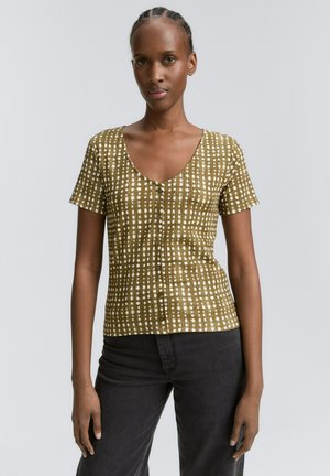Short-sleeve shirt in olive green with white dot pattern, V-neckline, and button closure at the front. Slightly textured fabric.