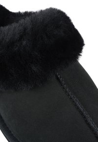 Black suede slipper featuring a plush, fuzzy black fur cuff and detailed stitching along the side, offering a soft texture and comfortable fit.