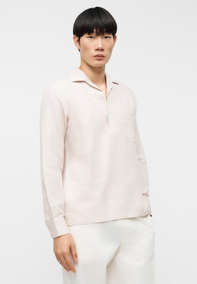 Ανοιχτό ροζ μακρυμάνικο πουκάμισο με γιακά, πόρπη με κουμπιά και τσέπη στο στήθος. Κατασκευασμένο από υφή ύφασμα, σε συνδυασμό με άσπρο παντελόνι.