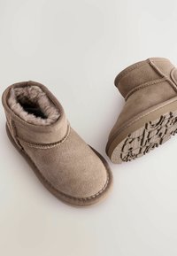 Beiga mockalädersstövlar med mjuk foder, rund tå, sydda detaljer och texturerad gummisula med ett mönstrat mönster.