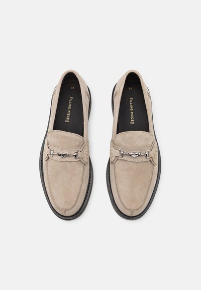Beige Wildleder-Slipper mit strukturierter Oberfläche, versehen mit einem silbernen Kettenakzent und einer schwarzen Gummisohle. Innenauskleidung für zusätzlichen Komfort.