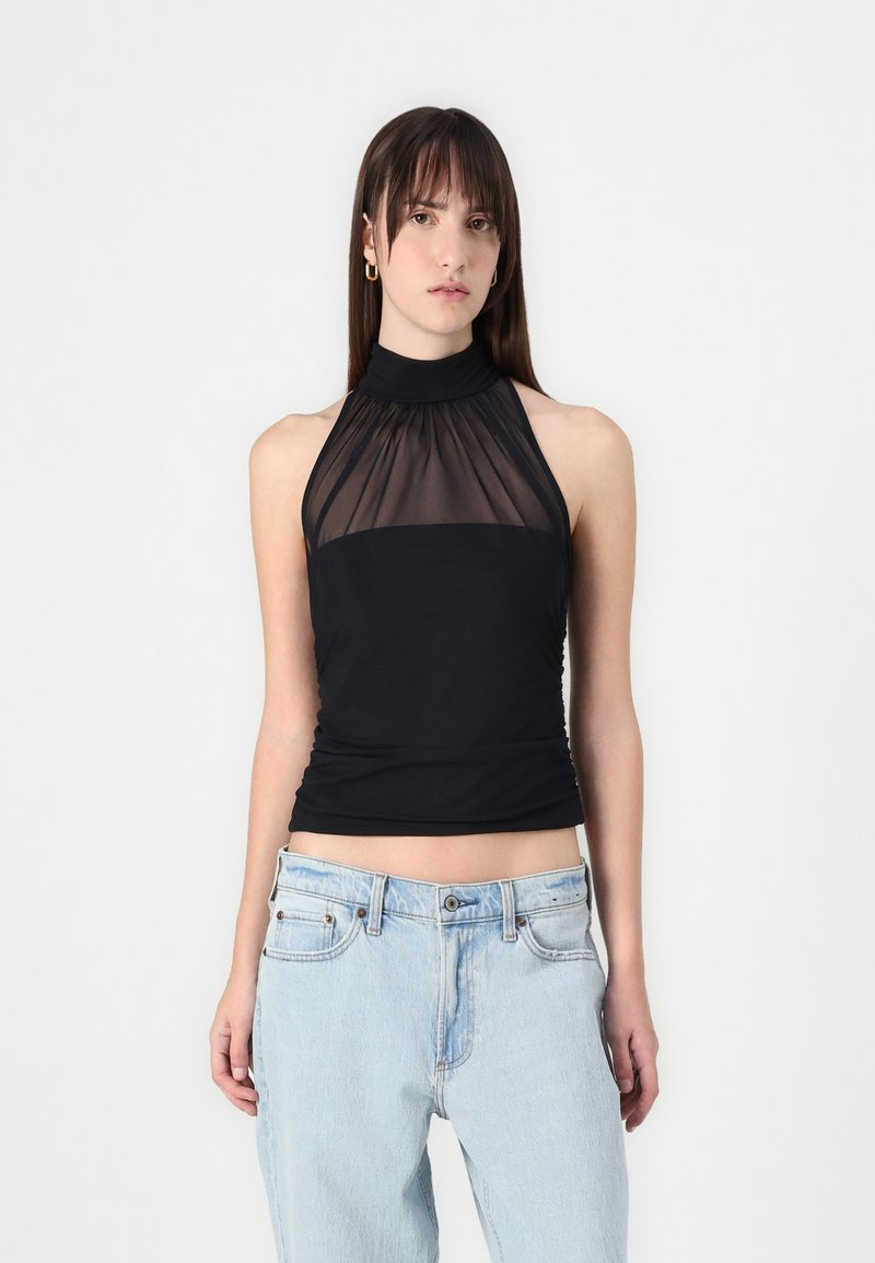 Schwarzes Halftertop mit transparenter Schulterpartie, gerafftem Hals und taillierter Passform. Kombiniert mit hellblauen, lässig geschnittenen Jeans.