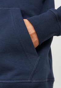 Sudadera azul marino con bolsillo tipo canguro, puños acanalados y una textura suave con detalles de costura visibles.