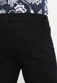 Svarta denimjeans med en slät textur, utrustade med en bakficka och sömdetaljer. Materialet är mjukt och figursytt.