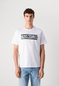 White cotton t-shirt featuring a black "CALVIN KLEIN NEW YORK" graphic on the front. Classic crew neck and relaxed short sleeves.