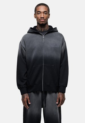 Black gradient zip-up hoodie with a front pocket, drawstring hood, and textured fabric. Features subtle logo detail on the chest.