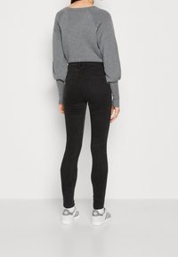 Vaqueros negros de cintura alta con un diseño ajustado, que presentan una textura suave y sutiles detalles de costura, combinados con una sudadera gris y zapatillas deportivas.