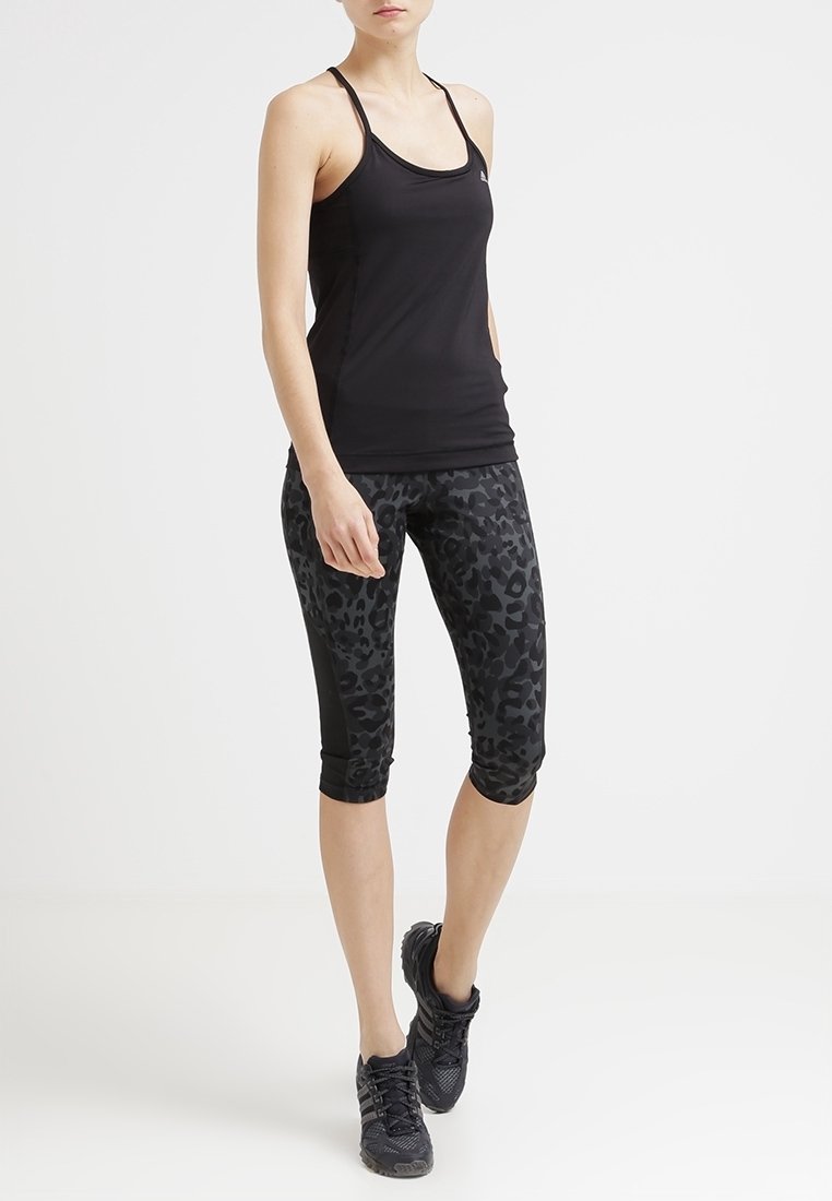 Top da allenamento nero con spalline sottili abbinato a leggings neri con stampa leopardata fino al ginocchio. La modella indossa scarpe sportive nere.