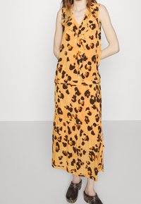 Abito leopardato in arancione e nero, con scollo a V, davanti arricciato e design a strati della gonna. Abbinato a zoccoli in legno scuro.