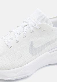 Baskets de sport blanches avec une tige texturée, un logo Nike gris clair, des détails en mesh et une semelle épaisse et rembourrée pour le confort.