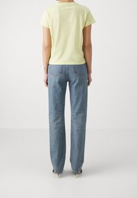 Gul kortärmad t-shirt i kombination med högmidjade ljusblå raka jeans. Tyget verkar mjukt, med en slät textur och enkel design.