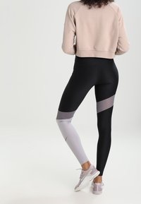 Leggings noirs et gris avec un design en blocs de couleur ; fabriqués en matière extensible. Portés avec un sweat-shirt court rose clair et des chaussures claires.