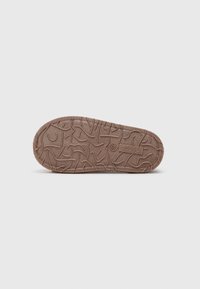 Suela de goma texturizada marrón con un patrón detallado de líneas entrelazadas, que presenta un logo en la parte inferior y una forma ligeramente redondeada.
