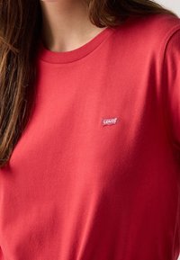 Czerwona bawełniana koszulka z okrągłym dekoltem i krótkimi rękawami, z małą białą naszywką logo Levi's na lewej piersi.
