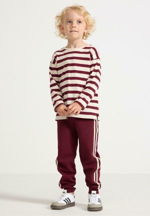 Lange mouw crèmekleurig shirt met bordeauxstrepen, gecombineerd met bordeaux joggers met crèmekleurige zijstrepen en witte sneakers met zwarte accenten.
