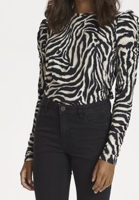 Langärmliges Oberteil mit schwarz-weißem Zebramuster und gepufften Schultern. Kombiniert mit hochgeschnittenen schwarzen Jeans.
