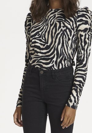 Langemouwige top met een zwart en crèmekleurig zebra-streepjespatroon, met opgeblazen schouders. Gepaard met high-waisted zwarte jeans.
