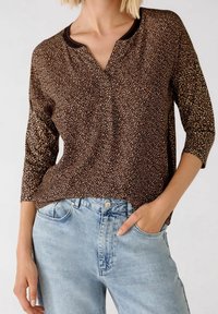 Top en imprimé léopard marron avec des manches trois-quarts, un col rond et des accents noirs, associé à un jean en denim bleu clair. Le matériau semble doux et texturé.