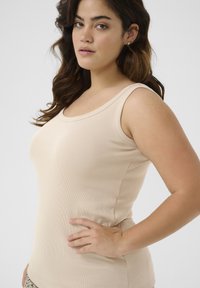 Beige geripptes Tanktop mit rundem Halsausschnitt und breiten Trägern, das eine taillierte Silhouette und eine glatte Textur aufweist.