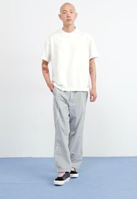 White short-sleeve t-shirt paired with light gray cargo pants featuring side pockets and white contrast stitching, finished with black sneakers.
