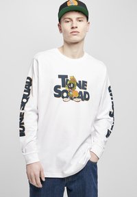 Hvit langermet skjorte med "Tune Squad" grafikk og en tegneseriefigur. Utsmykket med blå tekst på ermene; myk bomullsmateriale.