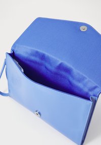 Borsa sintetica blu con una superficie testurizzata, un interno foderato di viola e una chiusura a scatto metallica rotonda. Include una tracolla.