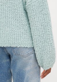 Ljusblå strukturerad stickad tröja med lös passform och ribbat avslut, kombinerad med denimjeans med glittrande silverdetaljer.