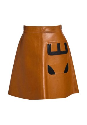 Jupe droite en cuir marron avec une grande poche frontale ornée de patches géométriques noirs sur fond blanc.