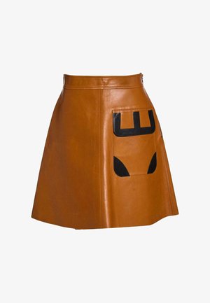 Jupe droite en cuir marron avec une grande poche frontale ornée de patches géométriques noirs sur fond blanc.