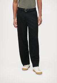Pantalon droit noir avec ceinture, fabriqu�é en tissu lisse, doté de poches latérales et d'une coupe confortable, associé à des chaussures blanches.