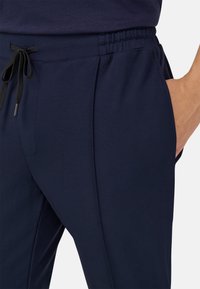 Tamsūs jogger tipo kelnių gaminys iš minkštos medžiagos, su elastingu juosmeniu ir juoda virvele, bei šoninėmis kišenėmis daiktams laikyti.